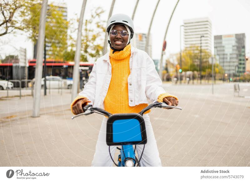 Lächelnde afrikanische Frau auf dem Fahrrad in einer Stadtlandschaft Großstadt Fahrradfahren urban Mitfahrgelegenheit Schutzhelm Brille heiter Wolkenkratzer