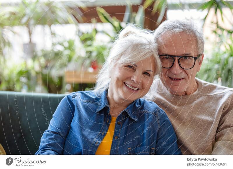 Porträt eines glücklichen älteren Paares, das zu Hause auf dem Sofa sitzt Menschen Kaukasier graue Haare lässig Tag im Innenbereich echte Menschen