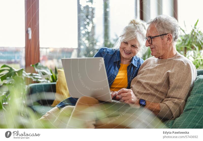 Älteres Ehepaar benutzt einen Laptop, während es auf dem Sofa im Wohnzimmer sitzt Menschen Kaukasier graue Haare lässig Tag Porträt im Innenbereich