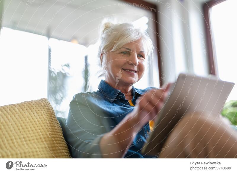 Reife Frau benutzt digitales Tablet, während sie zu Hause auf dem Sofa sitzt Menschen lässig Tag Porträt im Innenbereich echte Menschen weiße Menschen