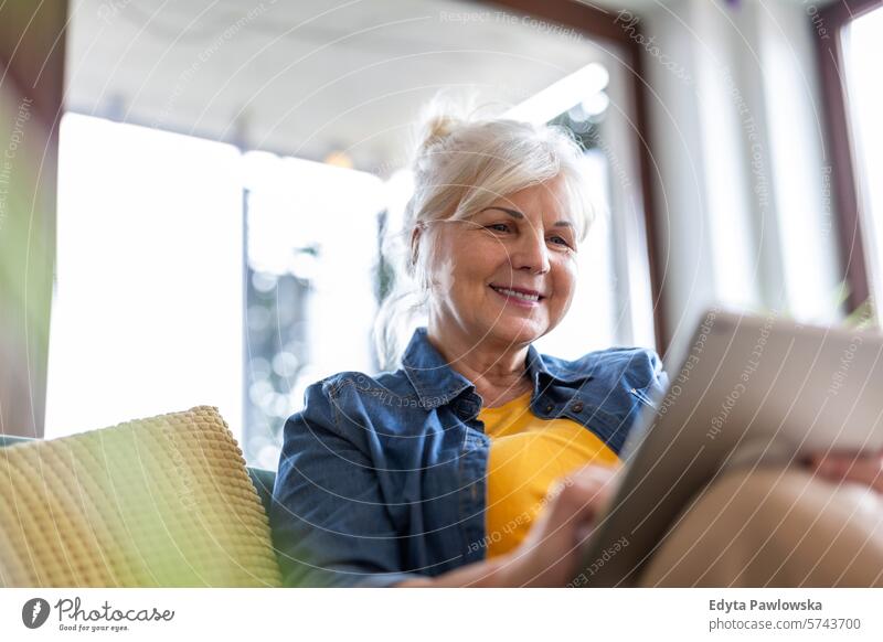 Reife Frau benutzt digitales Tablet, während sie zu Hause auf dem Sofa sitzt Menschen lässig Tag Porträt im Innenbereich echte Menschen weiße Menschen