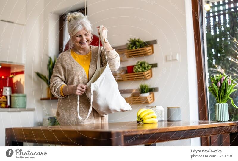 Ältere Frau hält wiederverwendbare Tasche mit Lebensmitteln in der Küche Tisch Einkaufstasche Früchte Gemüse Baumwolltasche Segeltuchtasche Textil