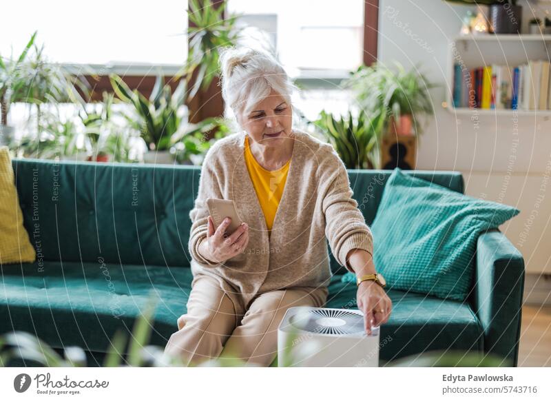 Eine ältere Frau benutzt ihr Smartphone, um einen Luftreiniger für zu Hause einzurichten Luftverschmutzung Technik & Technologie modern per Telefon Sofa