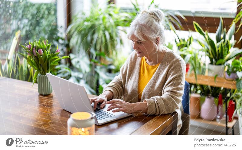Reife Frau, die einen Laptop benutzt, während sie zu Hause am Tisch sitzt Menschen lässig Tag Porträt im Innenbereich echte Menschen weiße Menschen Erwachsener