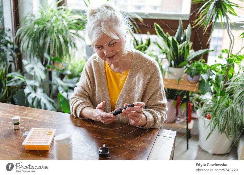 Ältere Frau prüft ihren Blutzuckerspiegel, während sie zu Hause sitzt Überprüfung Glaukometer Hände Tisch Gesundheit geduldig Krankheit Sitzen Blutzuckertest