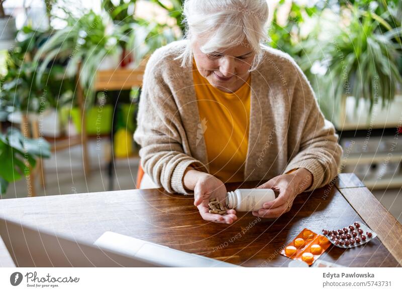 Ältere Frau nimmt Tabletten aus einer Flasche, während sie zu Hause am Tisch sitzt Menschen lässig Tag Porträt im Innenbereich echte Menschen weiße Menschen