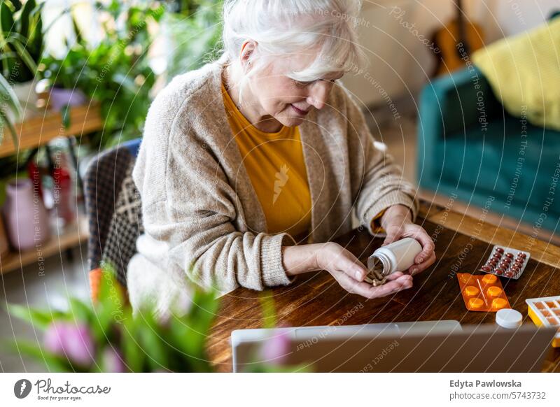 Ältere Frau nimmt Tabletten aus einer Flasche, während sie zu Hause am Tisch sitzt Menschen lässig Tag Porträt im Innenbereich echte Menschen weiße Menschen