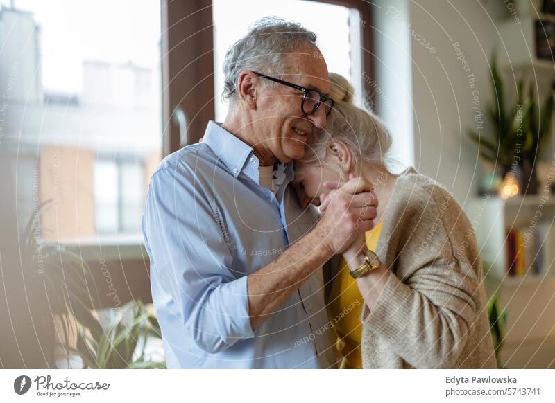 Glückliches älteres Paar tanzt im Wohnzimmer zu Hause Menschen Kaukasier graue Haare lässig Tag Porträt im Innenbereich echte Menschen weiße Menschen