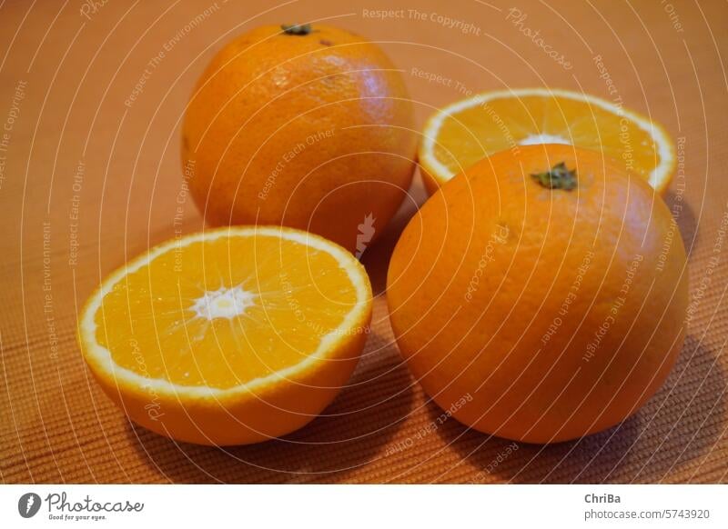 Orangen, teilweise halbiert auf orangefarbener Tischdecke Saft Saftorange frisch fruchtig lecker Lebensmittel Gesundheit Vitamin C Nahaufnahme Zitrusfrüchte