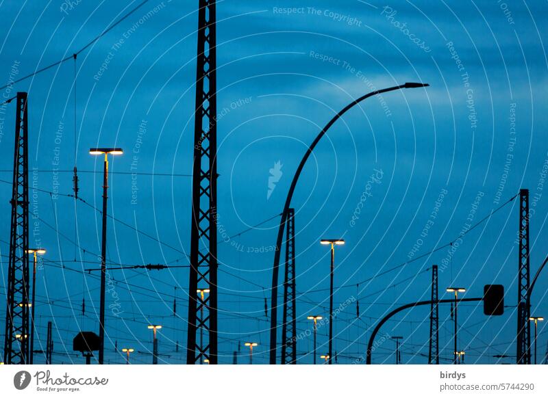 Oberleitungen und Beleuchtung einer Gleisanlage am Abend Stromleitungen Zugverkehr Elektrizität Bahnverkehr Blaue Stunde leuchten Lampen Masten Kunstlicht