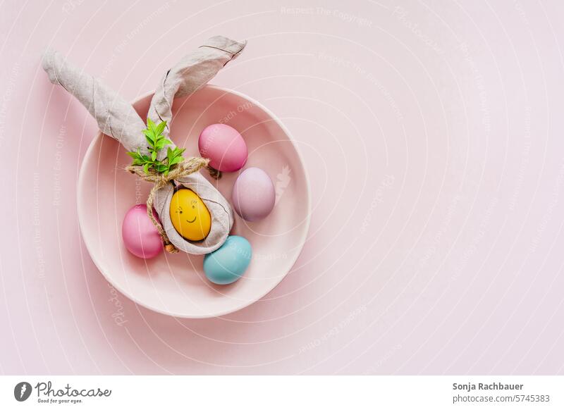 Ein gelbes Osterei mit Hasenohren aus einer Stoffserviette auf einem rosa Teller. Draufsicht. Ostern Kreativität Humor bunt Frühling Feste & Feiern mehrfarbig