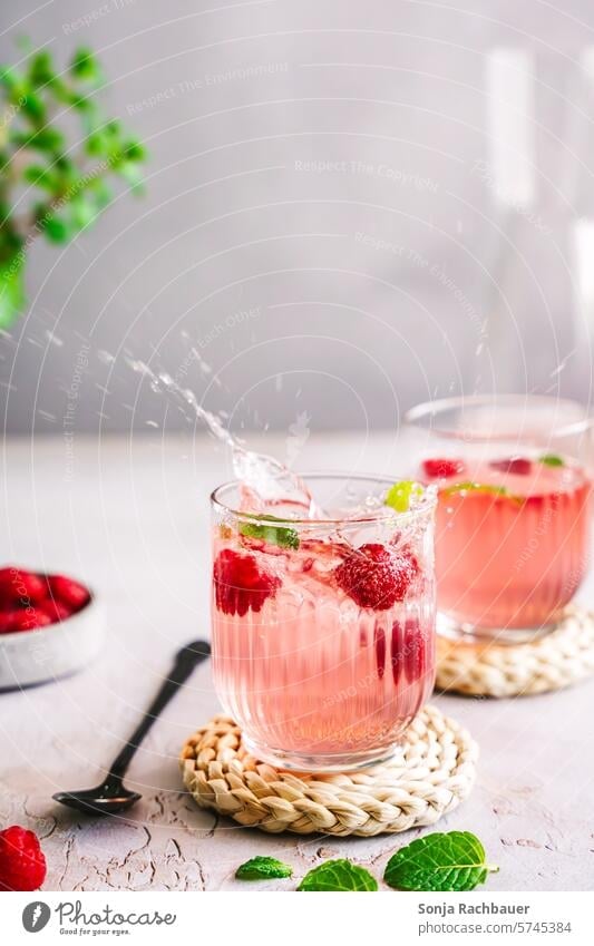 Spritziges Sommer Getränk mit Himbeeren in zwei Gläsern. Erfrischungsgetränk spritzig kalt Cocktail süß Limonade Longdrink Glas Farbfoto Alkohol Eiswürfel