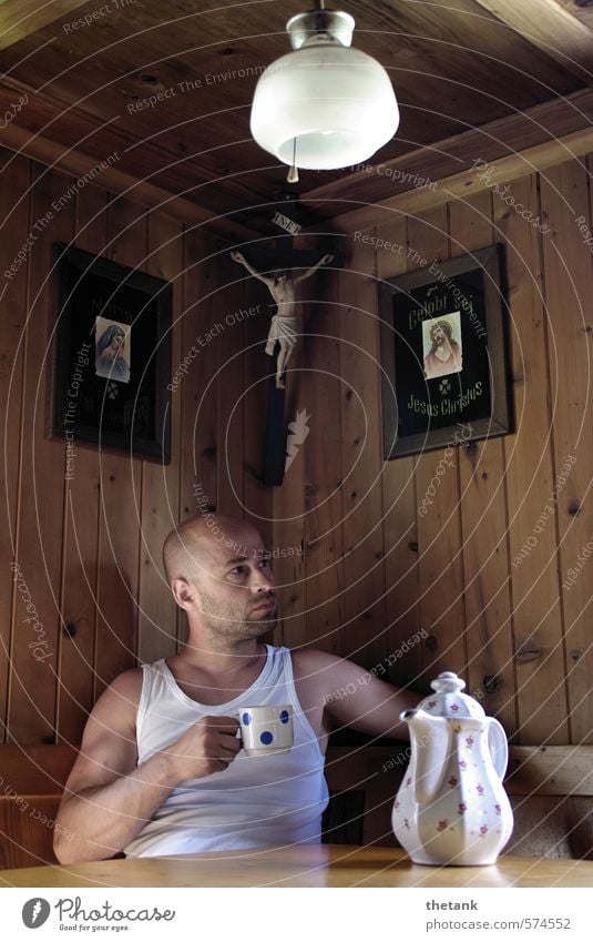 Ein Mann sitzt in einer Berghütte. Er hält eine Tasse in der Hand. Auf dem Tisch steht eine Kanne. trinken Kaffee Erholung ruhig Lampe Junger Mann Jugendliche