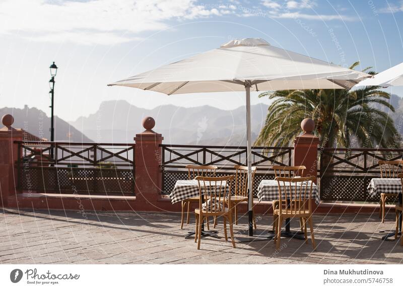 Restaurant- oder Caféterrasse mit Tisch und Stühlen und Sonnenschirm mit Blick auf die Berge Terrasse Menschenleer Gastronomie Straßencafé Stuhl Außenaufnahme