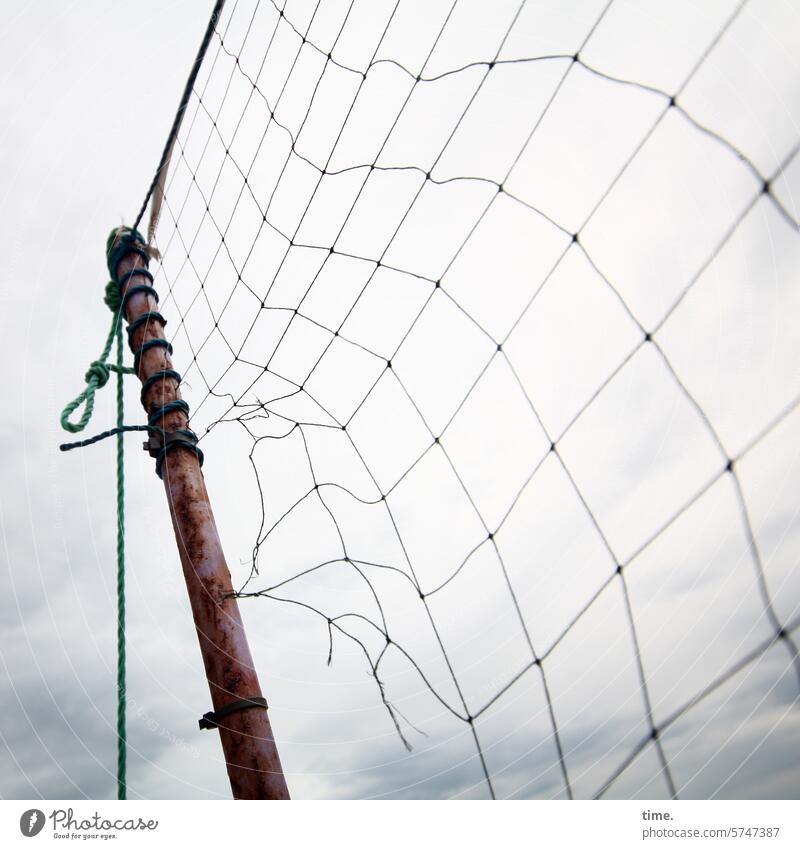 angerissenes Volleyballnetz an Holzstange vor bewölktem Himmel Wetter Wolken Landschaft Natur Perspektive Netz Spielgerät Beachvolleyball Seil Band Tau gebunden