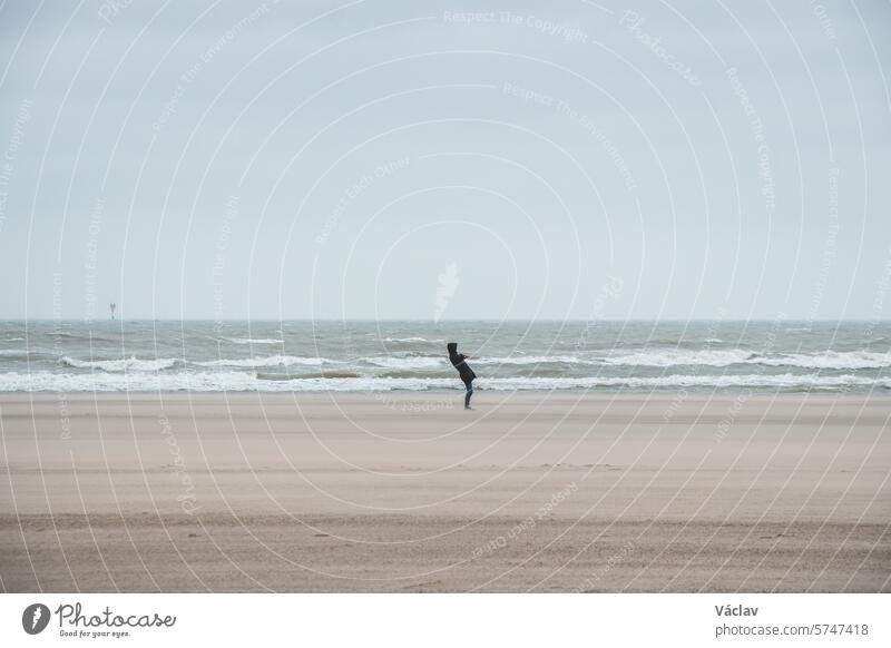 Ein Mann geht bei starkem Wind an einem Sandstrand in der Nähe von Blankenberge an der belgischen Westküste spazieren. Belgien erforschen und entdecken