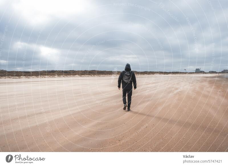 Ein Mann geht bei starkem Wind an einem Sandstrand in der Nähe von Blankenberge an der belgischen Westküste spazieren. Belgien erforschen und entdecken