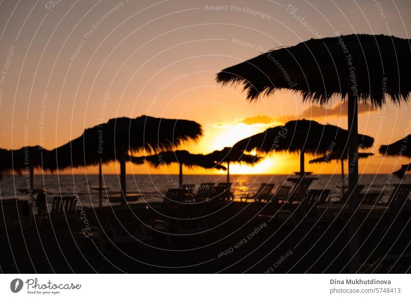 Sonnenuntergang am Strand mit Silhouetten von Juteschirmen und Liegestühlen. Reisen und Urlaub, entspannen. Regenschirm Sonnenliege Sonnenaufgang Landschaft
