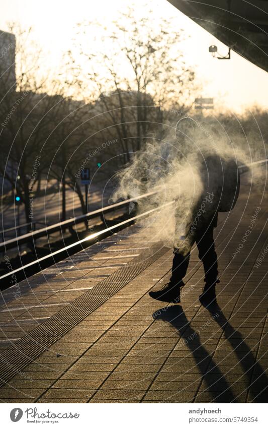 Ein rauchender Fahrgast auf dem Bahnsteig bei Sonnenaufgang Ankunft Zigarette Großstadt kalt gefährlich Abheben Europäer verboten Gesundheit ungesetzlich