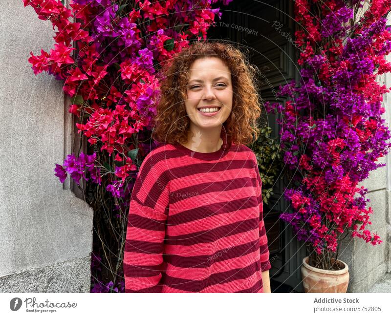 Lockenköpfige rothaarige Frau lächelt in einem bunten Stadtgarten Porträt Lächeln krause Haare floraler Bogen pulsierend urban Garten Glück heiter rosa Blumen