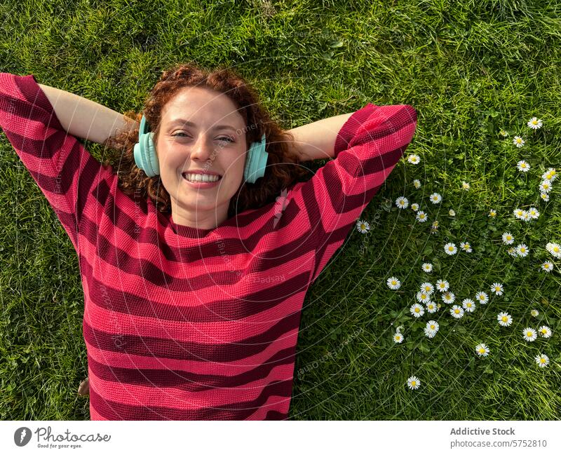 Junge rothaarige Frau entspannt sich mit Kopfhörern im Gras entspannend Margeriten heiter Genuss Musik Drahtlos liegend Lächeln Fröhlichkeit Freizeit im Freien