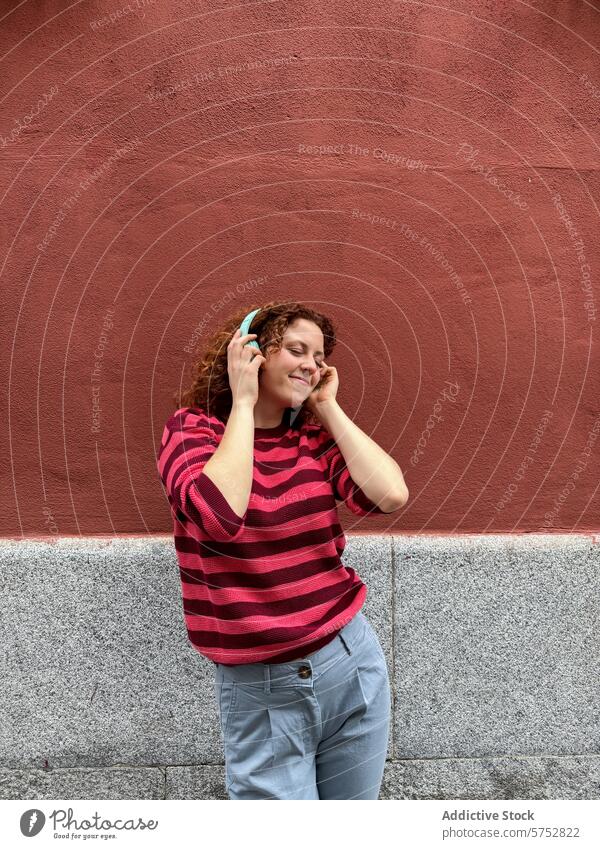Junge rothaarige Frau, die draußen Musik mit Kopfhörern genießt hören Lächeln Glück außerhalb Wand krause Haare blaugrün lässig Genuss Freizeit Lifestyle jung