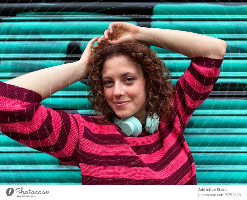 Junge rothaarige Frau mit Kopfhörern genießt die Stadtatmosphäre jung Lächeln Glück pulsierend blaugrün Hintergrund gestreift Pullover lässig urban Lifestyle