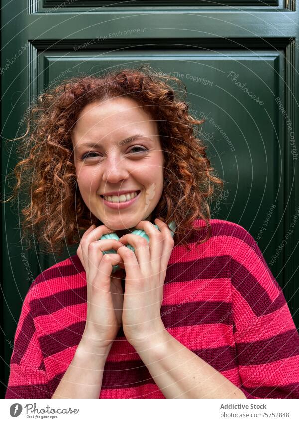 Lächelnde rothaarige Frau im gestreiften Pullover vor grüner Tür krause Haare rote Haare Streifenpullover grüne Tür Fröhlichkeit Mode Porträt junger Erwachsener