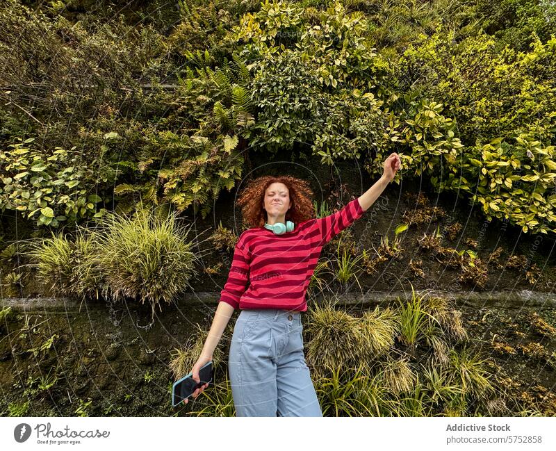 Junge rothaarige Frau genießt die Natur, umgeben von üppigem Grün Fröhlichkeit Freude Freiheit pulsierend Pflanzen Wand krause Haare strecken Waffen jung