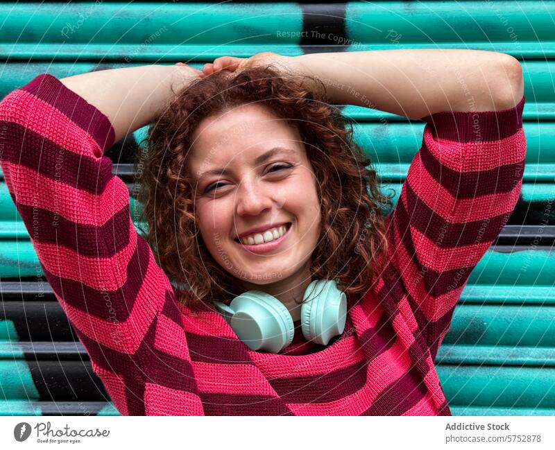 Fröhliche rothaarige Frau mit Kopfhörern genießt einen entspannten Moment Lächeln freudig pulsierend türkis Hintergrund Pullover gestreift heiter jung Mode
