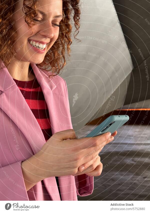 Rothaarige Frau in Rosa lächelt, während sie ein Smartphone in einem Haus benutzt Lächeln krause Haare rosa Blazer Freude Mitteilung Technik & Technologie