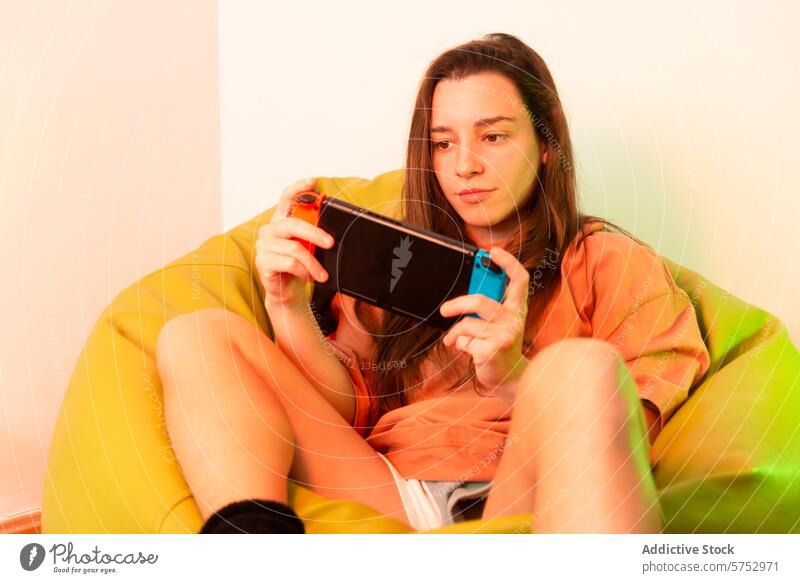 Eine fokussierte Person macht es sich in einem mehrfarbigen Sitzsack bequem, während sie sich mit einem Spiel auf einem tragbaren Spielgerät beschäftigt, das für gelegentliche Heimunterhaltung sorgt.