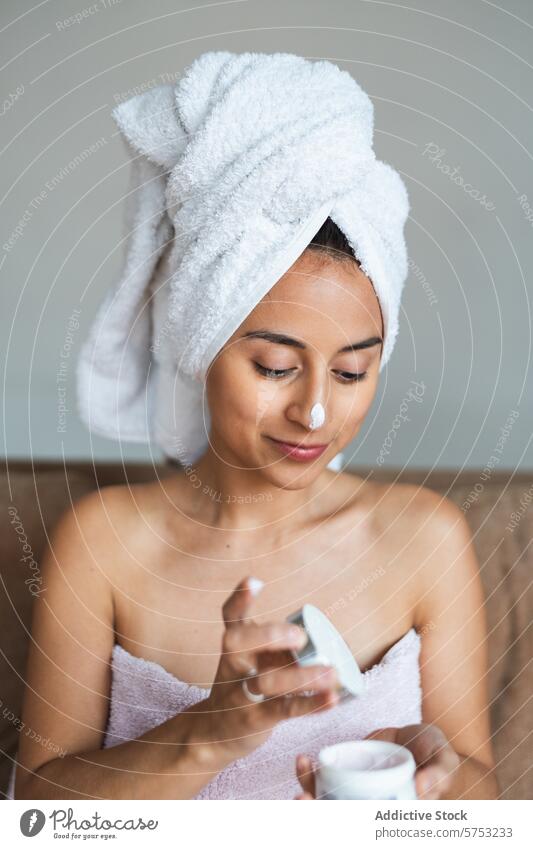 Junge Frau beim Eincremen des Gesichts zu Hause Hautpflege Gesichtsbehandlung Sahne feuchtigkeitsspendend Selbstfürsorge Schönheit Routine Handtuch Kopf