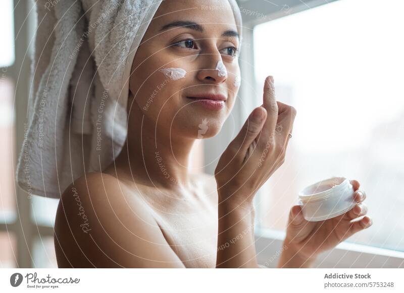 Frau trägt in einem gemütlichen Zimmer Feuchtigkeitscreme für das Gesicht auf Hautpflege Gesichtsbehandlung Sahne Schönheit Routine Morgen Handtuch Behaarung