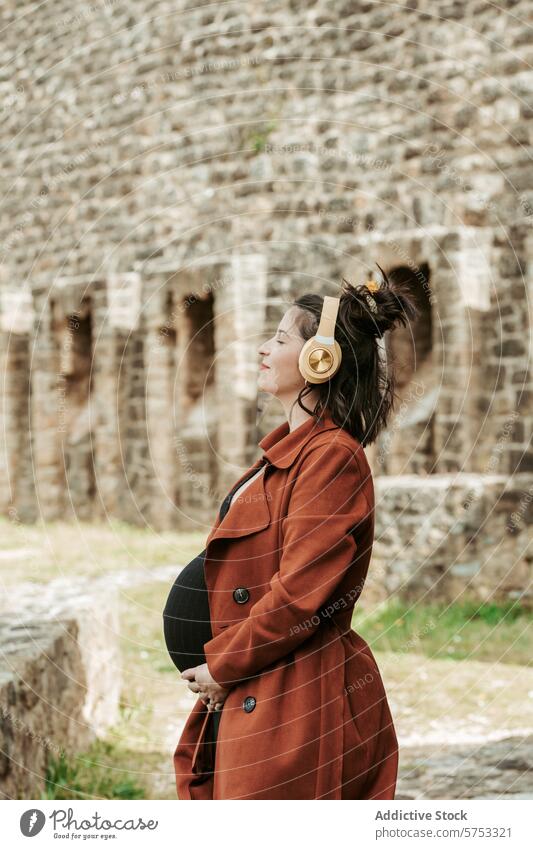 Werdende Mutter entspannt sich bei Musik im Freien Schwangerschaft Frau erwartungsvoll Kopfhörer Erholung Steinwand historisch Freizeit Genuss friedlich Stehen