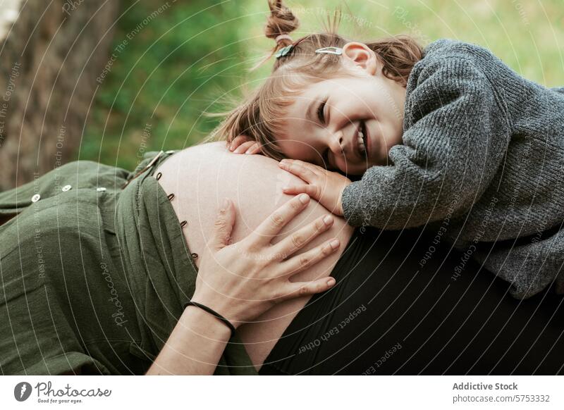 Kleines Mädchen lauscht dem schwangeren Bauch in der Natur Kind Schwangerschaft Mutterschaft Bonden Lächeln Familie im Freien Zuneigung jung Geschwisterkind