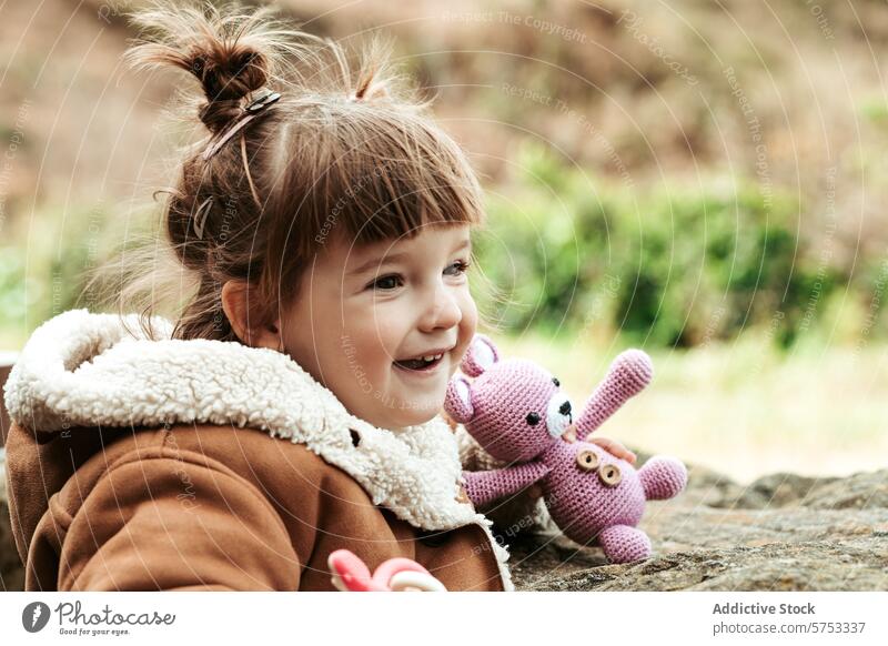 Lachendes Kind mit einem Plüschtier im Freien Mädchen Glück Spielzeug purpur Hase Natur Freude spielerisch Unschuld Kindheit Lächeln bezaubernd Fröhlichkeit