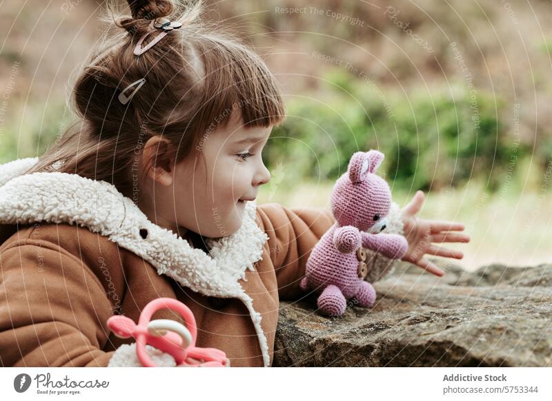 Junges Mädchen spielt mit einem gestrickten Hasen im Freien Kind spielen Vorstellungskraft Freude handgefertigt gefüllt Kaninchen Spielzeug gemütlich Jacke