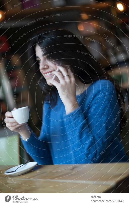 Frau beim Telefonieren in einem Cafe Gespräch Lächeln Kaffee Tasse Café im Innenbereich Sitzgelegenheit Tisch Holz lässig Mitteilung plaudernd sprechend Anruf