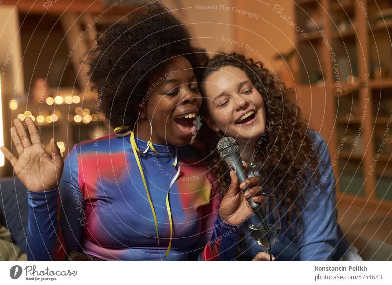 Waist up Porträt von zwei jungen Frauen singen, um Mikrofon und genießen Karaoke während home party Party heimwärts Menschen schwarze Frau Vielfalt
