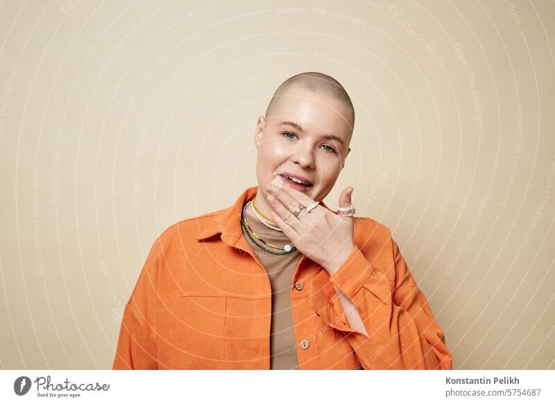 Porträt einer selbstbewussten jungen Frau mit Glatze und leuchtend orangefarbener Jacke im Studio kahl Mädchen gen z Haarausfall Alopezie Mund Lippen lutschen