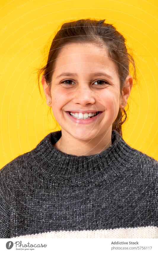 Porträt eines glücklichen jungen Mädchens mit einem strahlenden Lächeln, das einen gemütlichen Pullover trägt, vor einem lebhaften gelben Hintergrund Glück