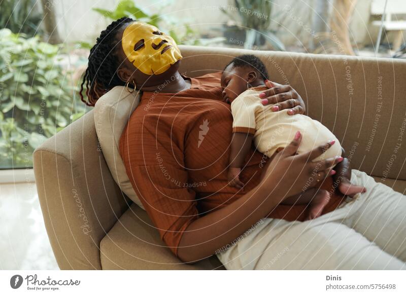 Black woman with moisturizing face mask on sleeping with her newborn baby asleep tired mother beauty infant girl calm motherhood little child care Black baby