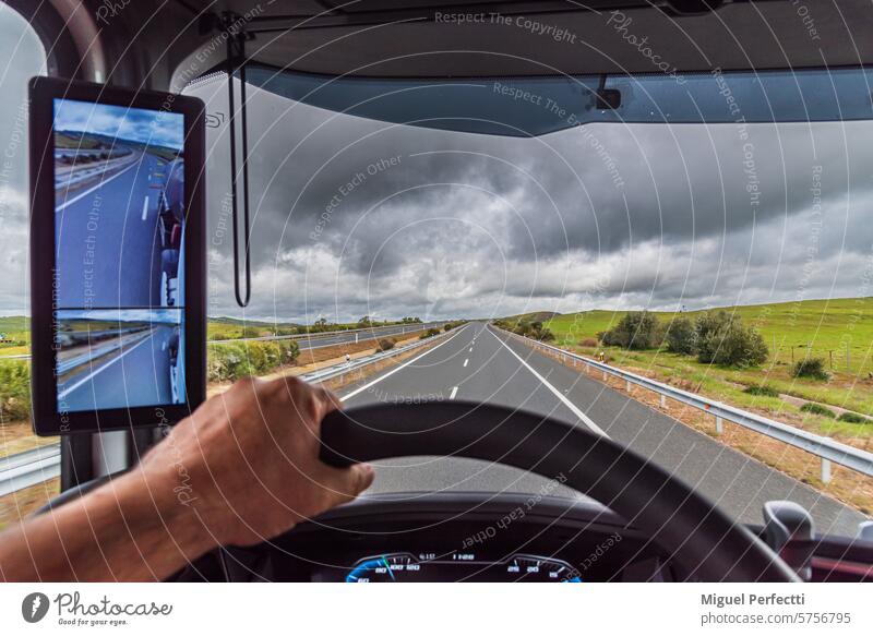 Blick aus dem Fahrersitz eines Lastwagens auf eine leere Autobahn unter einem drohenden Regenhimmel, ein Lastwagen mit einem Rückspiegel als Kamera. Straße