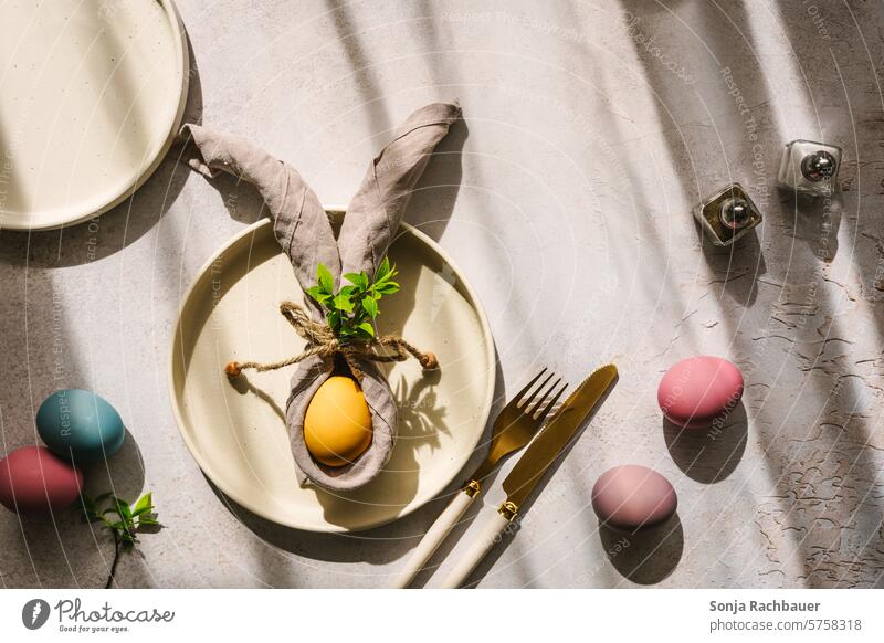 Ein gelbes Osterei mit Hasenohren aus einer Serviette auf einem Teller. Draufsicht. Ostern Osterhase Frühling Farbfoto hartes licht Schlagschatten Tisch