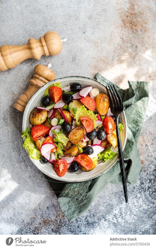 Draufsicht auf einen rustikalen mediterranen Kartoffelsalat mit Frühlingskartoffeln, schwarzen Oliven, Kirschtomaten, Frühlingszwiebeln, knackigem Kopfsalat und Radieschen, serviert mit einem Hauch von Eleganz