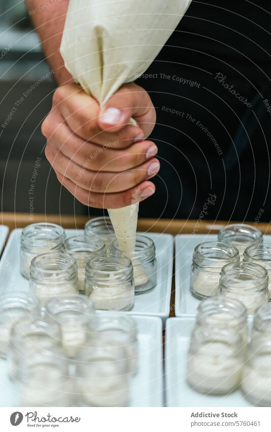 Nahaufnahme der Hände eines anonymen Kochs, der gekonnt Vanillecreme in kleine Gläser füllt und ein Gourmet-Dessert zubereitet Küchenchef Verrohrung Sahne