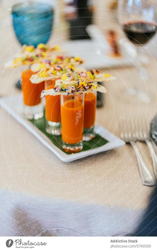 Eine kunstvolle Präsentation von Orangensuppen-Shootern mit üppig garnierten Crackern auf einer eleganten Tafel Suppe Schütze verziert Anzeige orange Abendessen