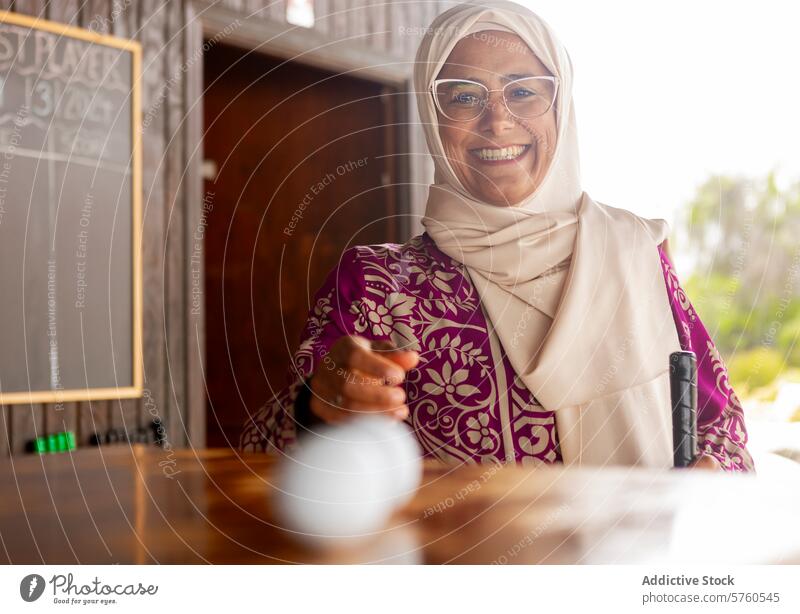 Fröhliche muslimische Frau bei einer Partie Minigolf heiter Lächeln Golfball Golfschläger Freizeit Aktivität Sport Spiel Erholung Fröhlichkeit Brille Genuss
