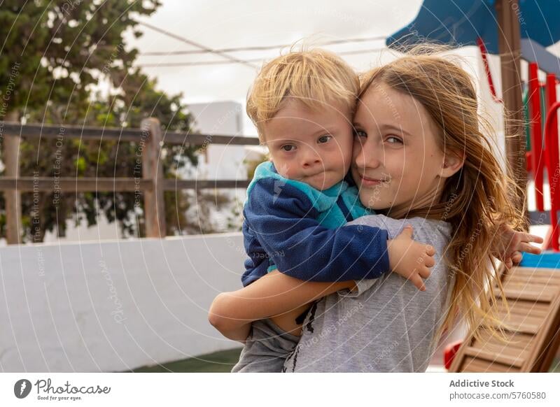 Geschwisterliebe auf dem Spielplatz mit einem Down-Syndrom-Kleinkind Baby Junge Mädchen Kind Bruder Schwester spielen Zuneigung Einschluss Vielfalt Umarmung